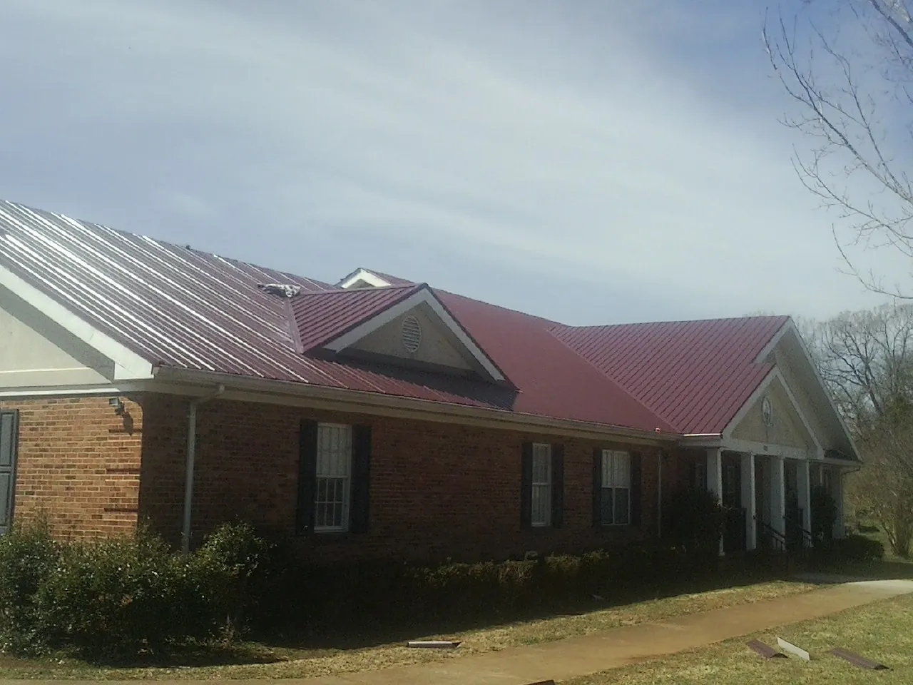Red metal roof with gabled entries on a long brick building, from a Hail Damage Roof Repair job in Buckley