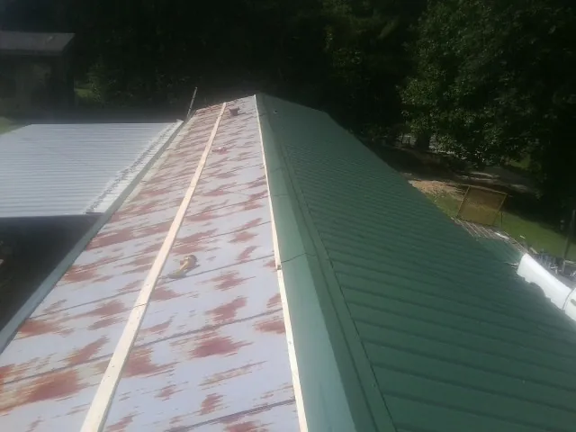 Old rusted panels beside newly installed green metal roofing — Wind Damage Roof Repair by Roofing Brothers in Buckley