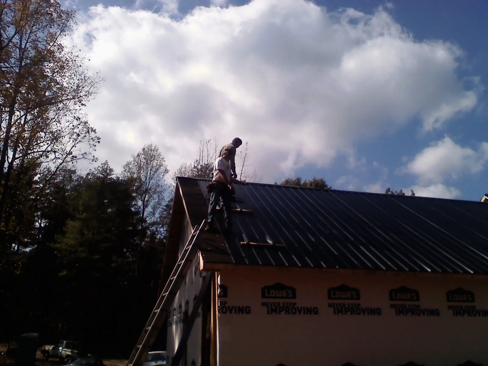 Roofer fastening dark metal panels high against a cloudy sky in Buckley